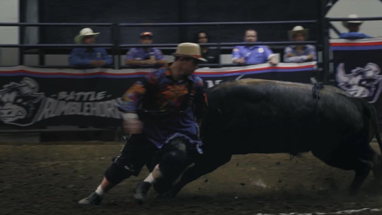 A bullfighter takes a black bull shoulder-first in front of the Battle of the Rumblehorn banner